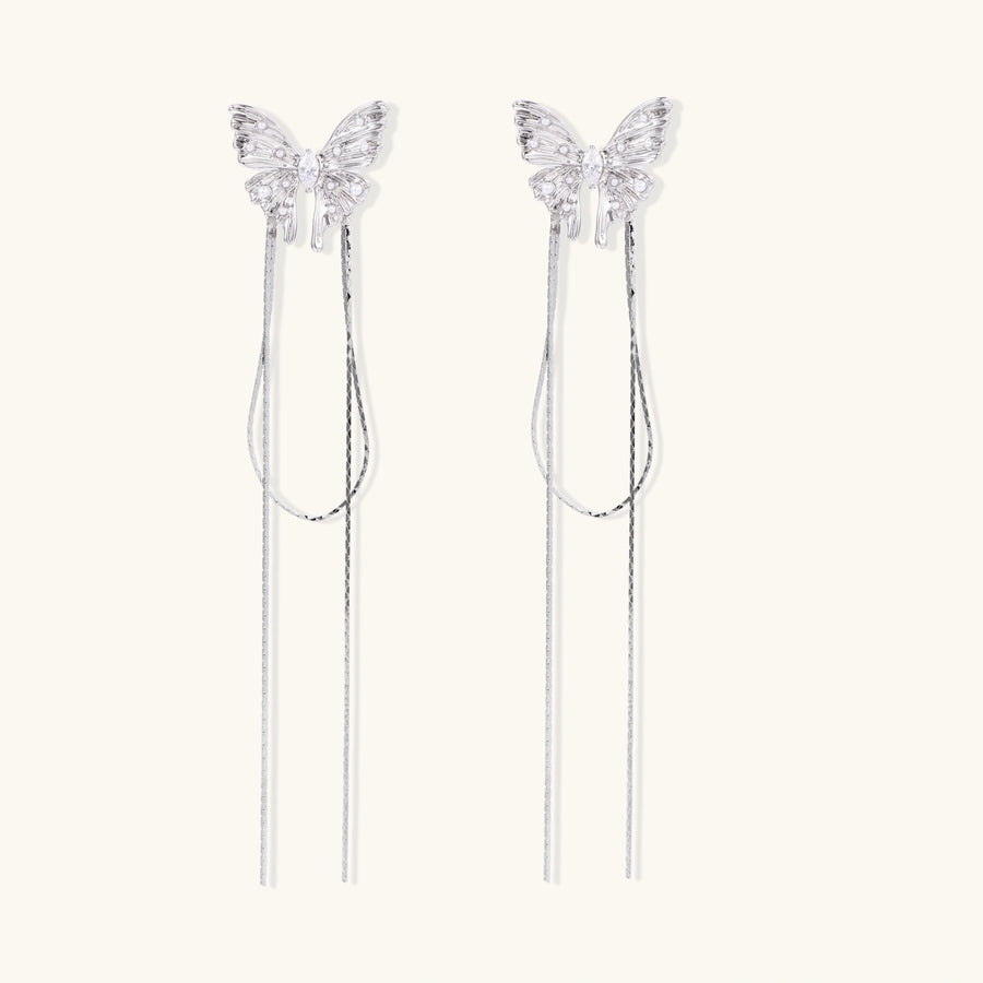 Pair of silver threader earrings with crystal butterfly tops and long chain drops on cream background.