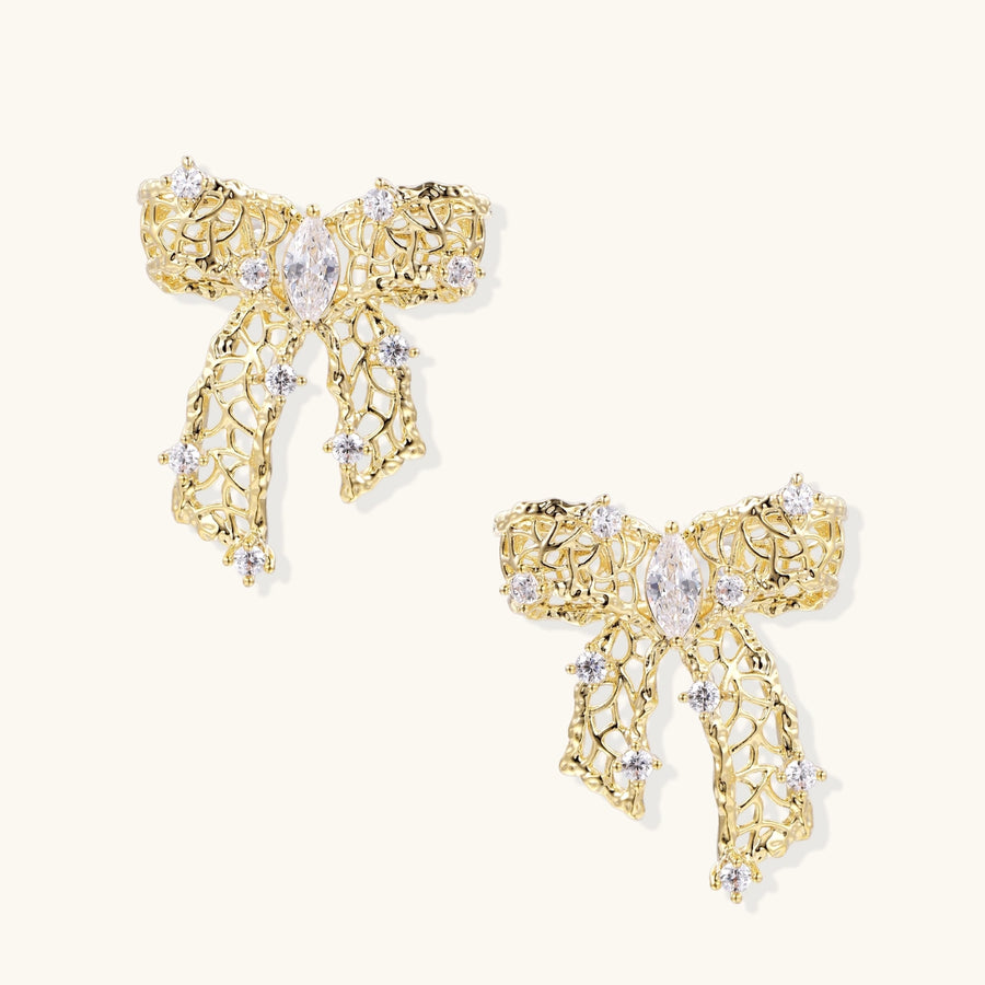 Gold-plated bow earrings with openwork design, marquise center stones, and flowing ribbon tails adorned with zirconia crystals.