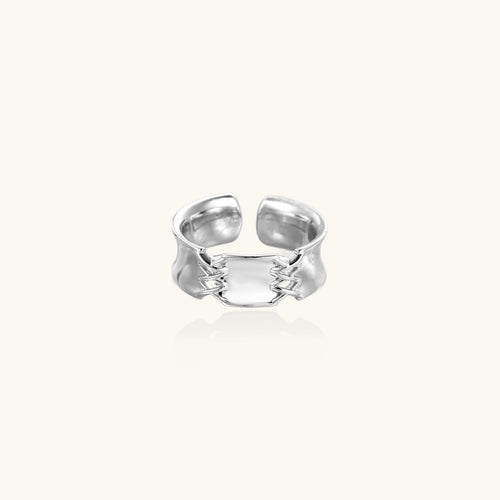 Adjustable silver-toned ring with sculptural stitch design across polished white gold-plated brass band